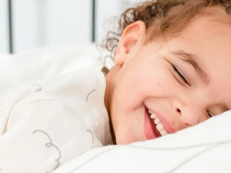 Curly-haired preschooler laughing in a big-kid bed, happy preschooler bedtime