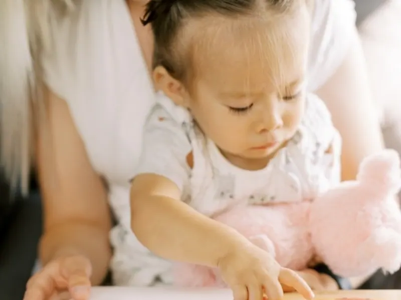 Toddler on a parent’s lap turning the pages of a picture book, a calm toddler bedtime routine