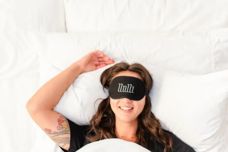 Smiling woman in bed wearing a sleep mask, rested after busting baby sleep myths