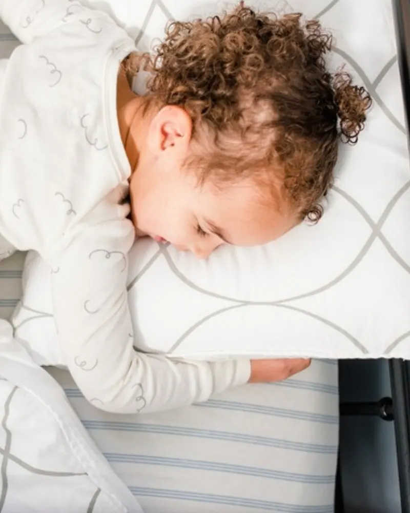 Curly-haired preschooler asleep face-down on a pillow in a big-kid bed after a calm bedtime